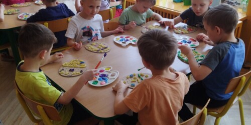 Dzieci przy stolikach z paletą farb i pisankami