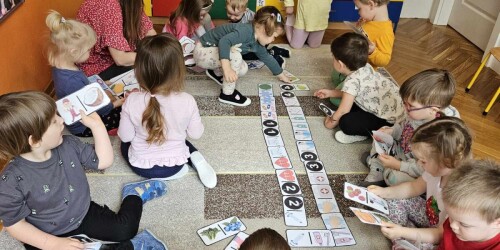 Dzieci w kole na dywanie układają mega domino