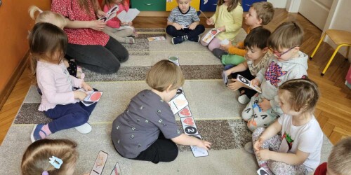 Dzieci z nauczycielką układają domino na dywanie